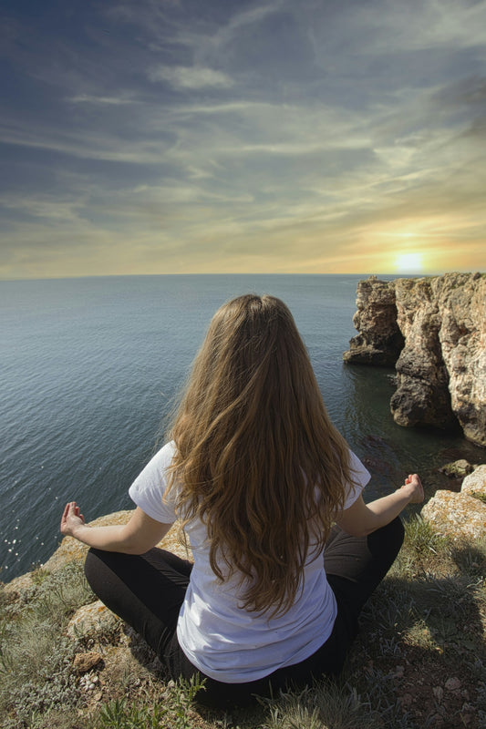 woman meditating on high mountain ground near sea during daytime