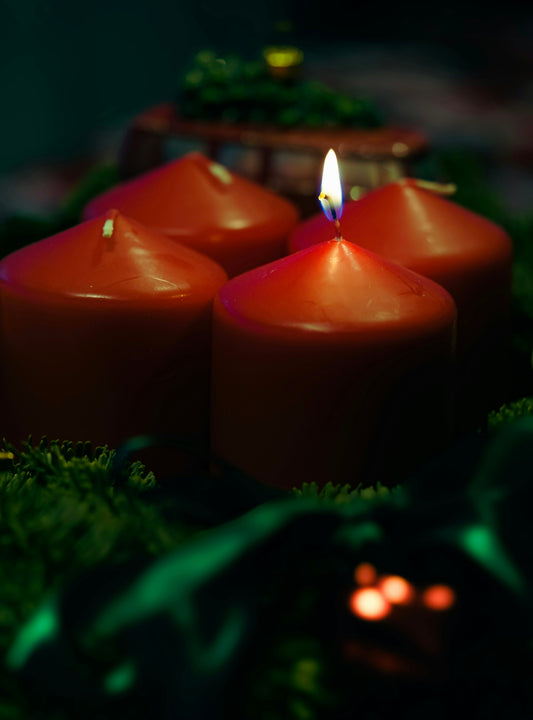 Three red candles sitting on top of a lush green field